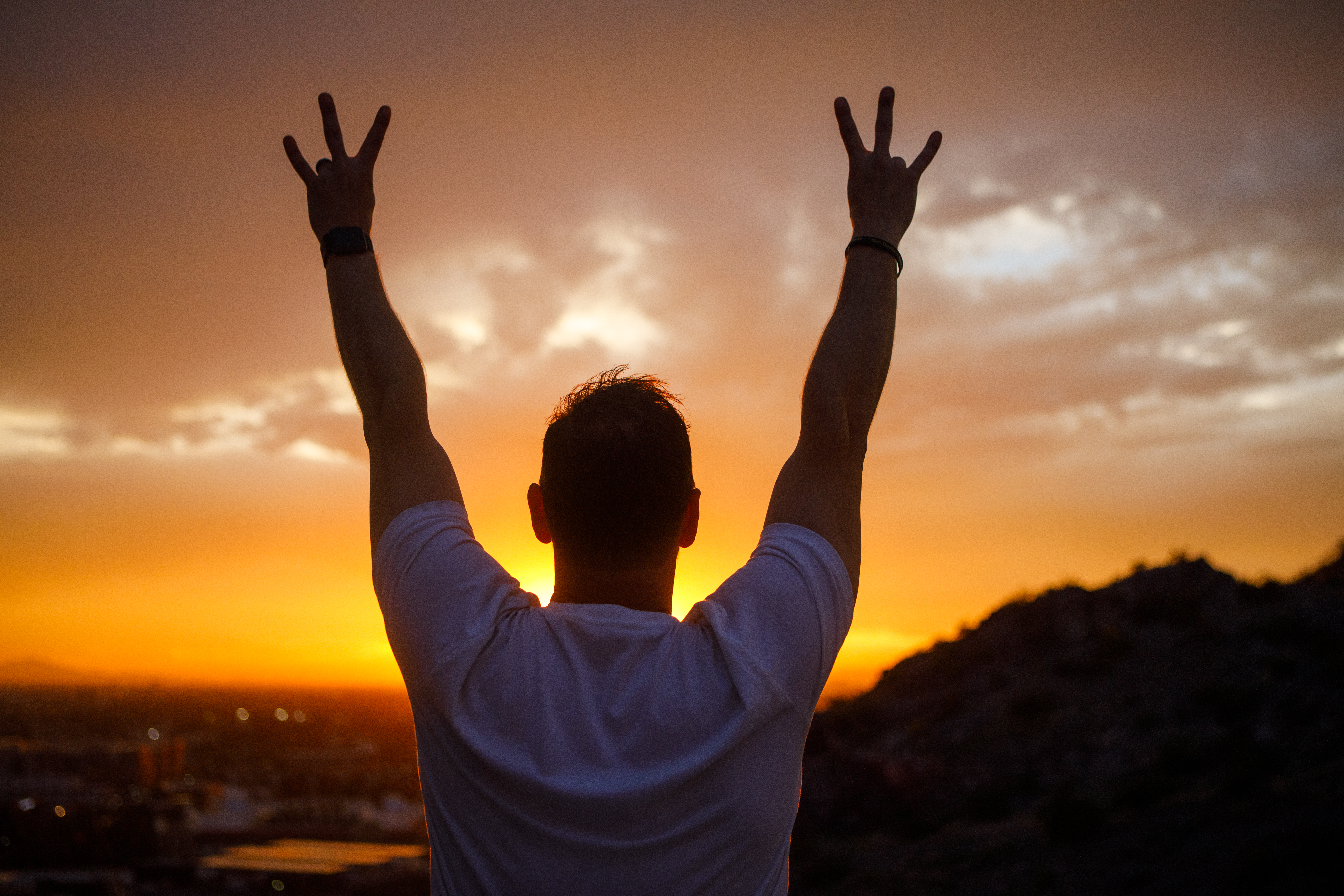Man holding the asu pitchfork hand symbol with a sunset behind him